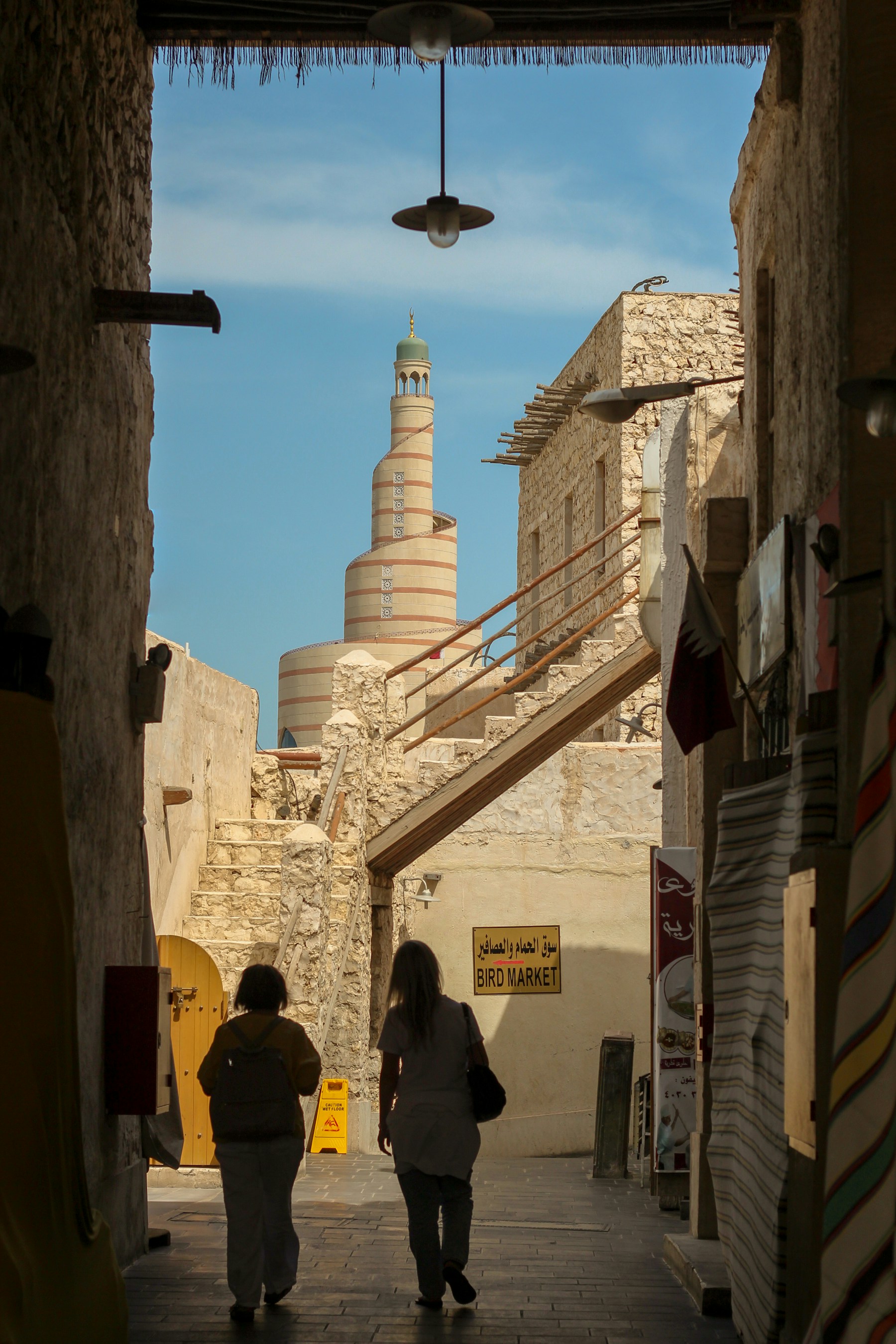 People walking through Souq Waqif, with stone walls and Arabic shop signs